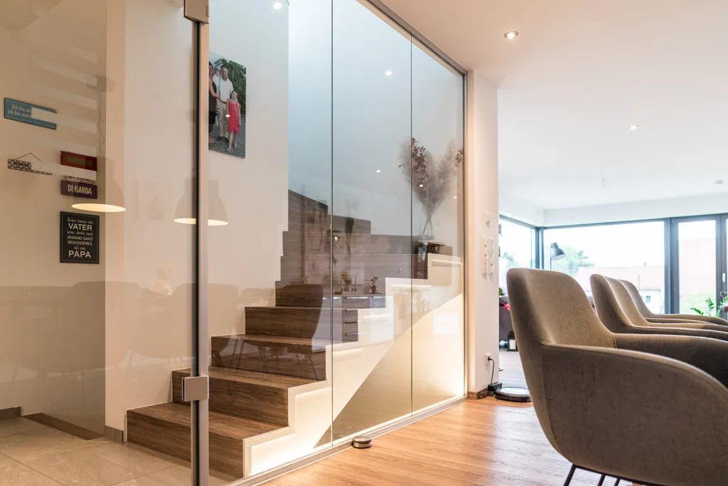 Treppe mit Glasgeländer neben einer hinterleuchteten Garderobenwand